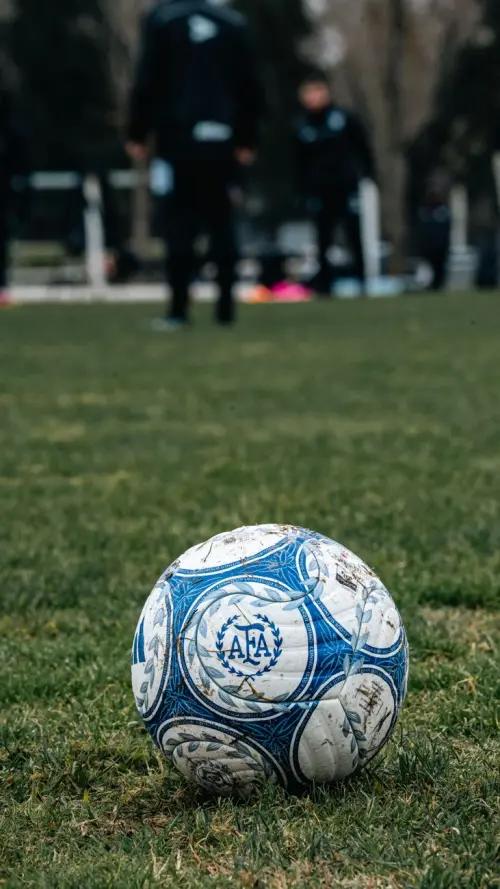 Close-up of a soccer ball on a grassy field during a practice session, suggesting teamwork and training.